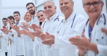smiling female doctor standing in front of her applauding colleagues.