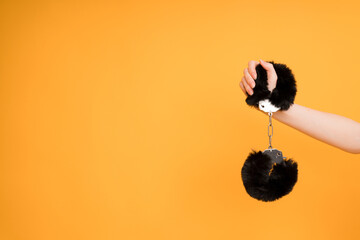 Close-up of a female hand with black handcuffs from a sex shop for adult games on an orange...