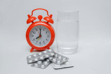 Red alarm clock with a glass of water and pills in a blister on a white background with a blank space for text, health concepts, medication regimens, treatment, vitamins and antibiotics