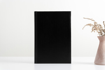 Black book mockup with workspace accessories, dried flowers in vase. Front view. Place for text, copy space, mockup