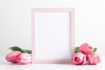 Flowers composition romantic. Pink photo frame mockup with pink tulips, spring flowers on white table. Front view. Place for text, copy space, mockup