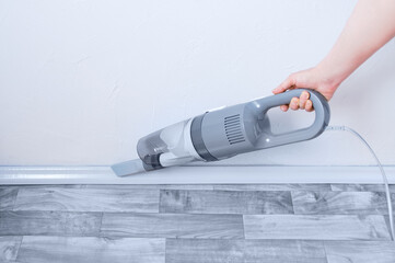 Handheld gray vacuum cleaner in the hand of  caucasian woman. Vacuuming the skirting board.