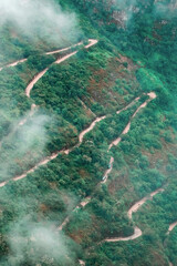 Aerial view of mountain forested serpetine road coverd with clouds