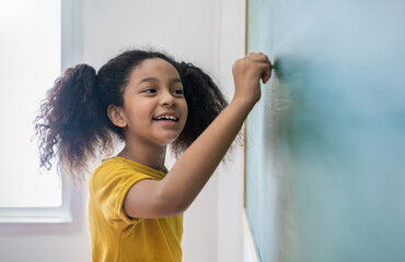 Closeup portrait of young happy African little girl write on chalk board. student writing on...