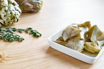 Artichokes hearts marinated with olive oil and herbs. Pickled artichoke with garlic in white plate on wooden table. Homemade healthy eating.