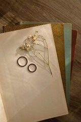 Pressed gypsophila flower, golden wedding rings and stack of beautiful vintage books on the table. Top view.