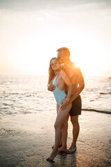 Fototapeta na wymiar A loving couple walks along the beach by the sea. Young family at sunset by the Mediterranean Sea. Vacation concept. A woman in a swimsuit and a man in shorts at sunset by the sea. Selective focus.