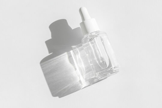 Transparent liquid product packaging in glass bottle. Anti aging serum with collagen and peptides on white with sunlight and shadow. Hyaluronic or polyglutamic acid oil cosmetic mockup. Flat lay.