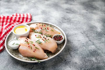 Chicken fillet with herbs and spices on gray table close up. Chicken meat with ingredients for cooking. Copy space.