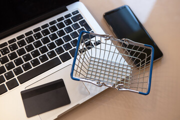 Shopping cart, laptop, mobile phone, credit card on the desktop. Top view, soft selective focus. Online shopping concept, e-commerce, self-isolation, banking financial transactions