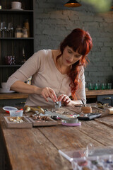 Red haired woman craftsman manufacturing jewelry in her workshop, handicraft process of making rings on wooden table