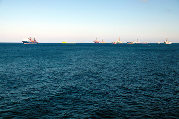 Obraz premium Oil rigs, tugs and various service ships anchored in the outer harbour waiting for refueling and repair.