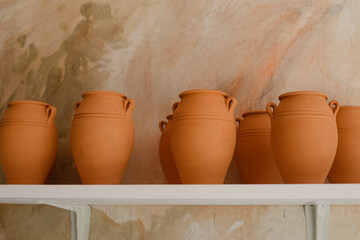 Clay jars stand on a white shelf.