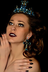 A princess.Girl with a crown decorated with precious stones sitting in studio on light background. Dark lipstick