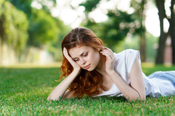 red-haired woman lies in the park on the lawn in the fresh air