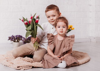 Naklejka premium Boy and girl, brother and sister sit in a white room with flowers