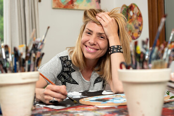 Fototapeta premium young latin woman plastic artist painter very happy in her art studio with her canvases and brushes