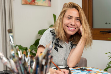 young latin woman plastic artist painter very happy in her art studio with her canvases and brushes