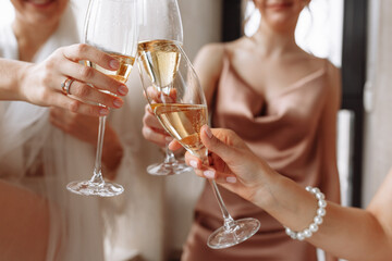 Morning of bride. Gorgeous bride with best bridesmaids are holding glasses and drinking champagne in hotel bathroom near the window. Sexy bridesmaids in exciting negligee. Wedding morning details