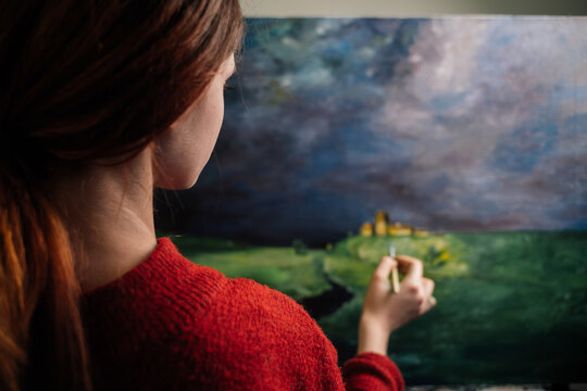 a woman paints a picture with bright paints on canvas and a brush in her hand