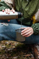 The girl pours aromatic tea from a thermos in the forest.