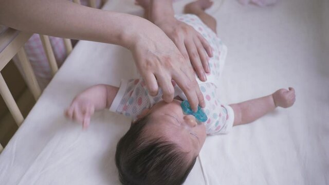 cropped shot newborn baby lying in the crib is getting irritated while given a pacifier and being patted on the chest by her caretaker.