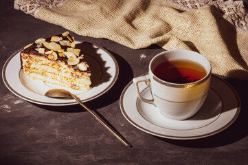 Still life - layered homemade sponge cake and a cup of black tea in a white dish, and a linen...