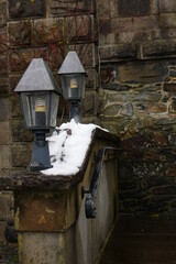 black metal lanterns on an old stone wall covered with snow as a stair railing in front of a wall with old large stones