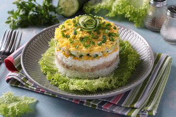 Festive salad with cod liver, rice, eggs, corn and cucumber on a plate on light blue background.