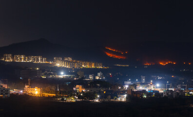 Fototapeta na wymiar Night view of the city, controlled brush fire in the hills at the backdrop.