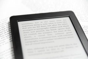 Detail of an electronic reader with text on the screen, on printed paper sheets