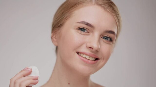 Young woman washing her face by sponge. Close-up portrait smiling blonde female. advertising fresh clean healthy skincare concept. Adorable young half-naked woman removing makeup with a cotton pad.