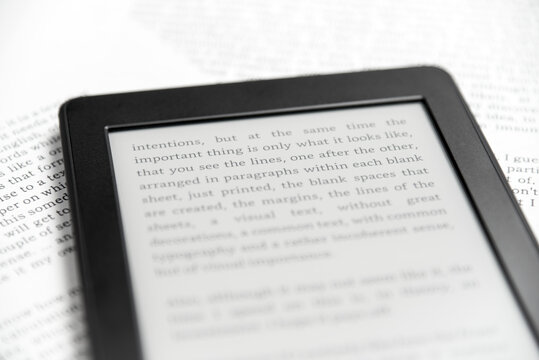Detail of an electronic reader with text on the screen, on printed paper sheets