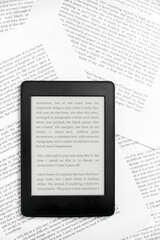 Fototapeta premium Electronic reader with the screen on and a text on it, on paper sheets.