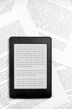 Electronic reader with the screen on and a text on it, on paper sheets.