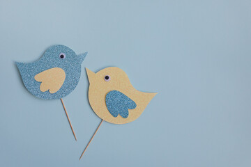 Cute paper Easter birds of blue and yellow color on a light-blue background. Easter birds are attached to a stick. Creativity concept. Easter decor.