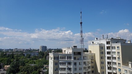 Fototapeta na wymiar White clouds in blue sky over city high-rise buildings and communication tower antenna in residential district of European city