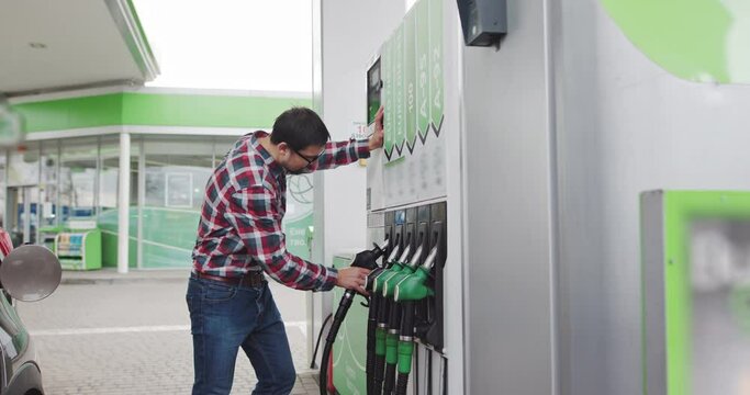 Man Takes A Fuel Pistol To Refuel The Car. Portrait of a Young Man in Glasses, Stylishly Dressed, Holding a Car Refueling Gun. Shooting At the Gas Station. Gasoline, gas, fuel, petroleum concept.