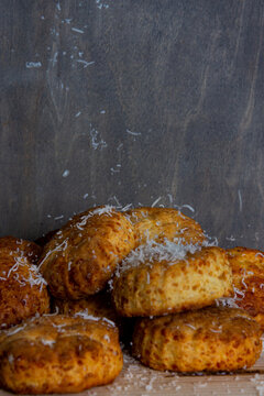 A Pile Of Cheese Scones Being Dusted With Grated Parmesan Cheese Against A Grey Background. 