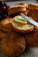 A close up view of a buttered cheese scone and knife positioned atop others and dusted with...