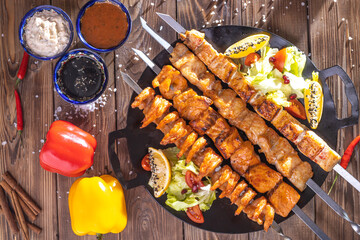 Minced kebab on a metal skewer with sauce, sliced cucumbers, tomatoes and onions.