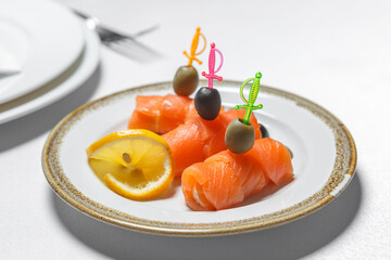 Red fish on skewers with olives and lemon is on a plate.