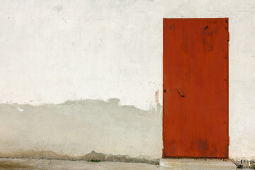 A red metal door in the plastered wall of a stone house.