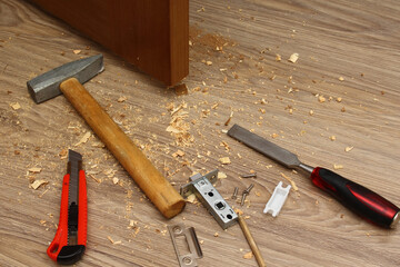 Shavings on floor from door latch installing. Wood sawdust from hole for door lock making. Hammer,...