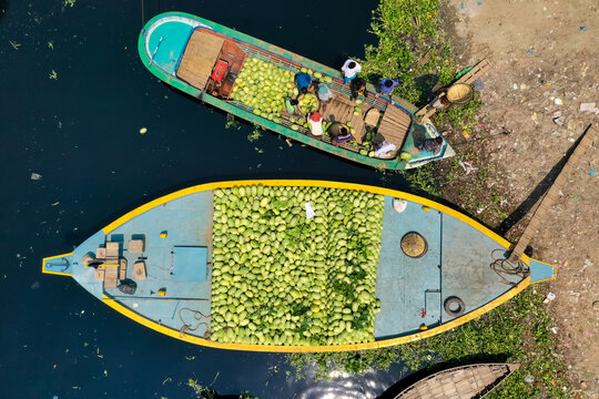 Aerial view of several small commercial boats with people unloading watermelons at Old Dhaka river port along Buriganga river in Dhaka, Bangladesh.