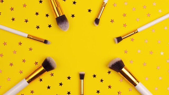 Stop motion animation of gold colored  cosmetics white brushes set for makeup and stars on bright yellow background. Cosmetics and beauty concept template Make up concept with copy space flat lay.