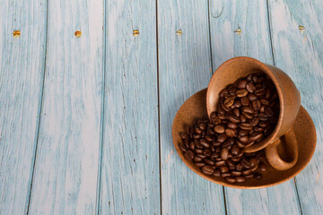 Coffee beans are scattered from an inverted cup on a saucer. The cup is on the right against a...