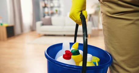 Close up shot of person hand in yellow gloves holding bucket with many different products and items for cleaning, business concept, cleaning service, clean up apartment, domestic tools