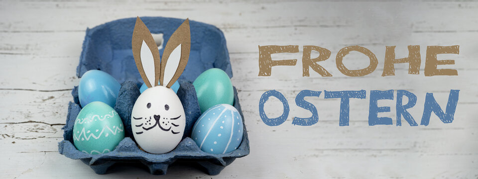 Frohe Ostern Hintergrund Banner Panorama Gru&szlig;karte - Nahaufnahme von bunten bemalten Eiern und Osterhase in blauem Eierkarton auf rustikalem wei&szlig;en Vintage shabby Holztisch