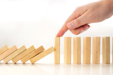 A person stopping wooden pieces of a domino effect. Concept: Business crisis and risk protection...
